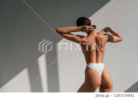 Without bra. Showing back. Young caucasian woman with slim body shape is indoors in the studio 126314991
