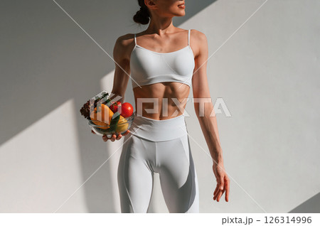 Holding vegetables and fruits. Young caucasian woman with slim body shape is indoors in the studio Holding vegetables and fruits. Young caucasian woman with slim body shape is indoors in the studio 126314996