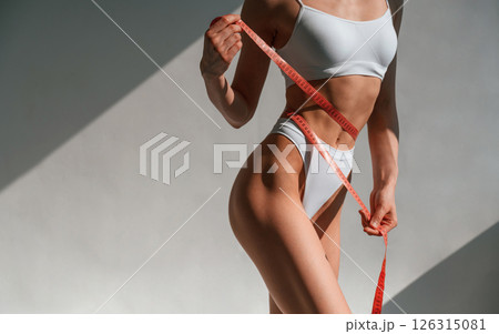 Close up view of woman that is holding measuring tape in hands. Standing in the studio Close up view of woman that is holding measuring tape in hands. Standing in the studio 126315081