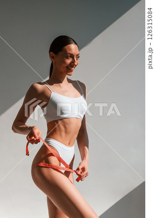 Weight loss conception. With measuring tape. Young caucasian woman with slim body shape is indoors in the studio 126315084
