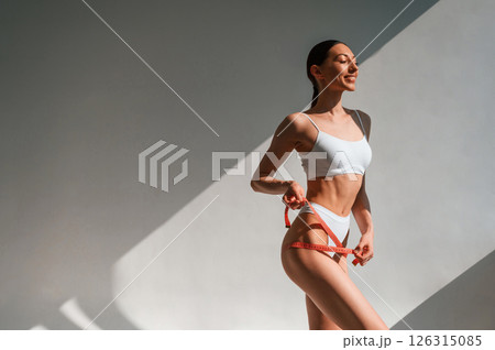 Weight loss conception. With measuring tape. Young caucasian woman with slim body shape is indoors in the studio 126315085