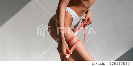 Close up view of woman that is holding measuring tape in hands. Standing in the studio Close up view of woman that is holding measuring tape in hands. Standing in the studio 126315089
