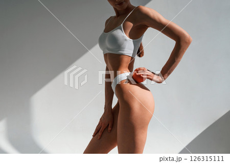 With an orange in hand. Young caucasian woman with slim body shape is indoors in the studio With an orange in hand. Young caucasian woman with slim body shape is indoors in the studio 126315111