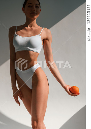 Orange fruit is in the hand. Young caucasian woman with slim body shape is indoors in the studio Orange fruit is in the hand. Young caucasian woman with slim body shape is indoors in the studio 126315125