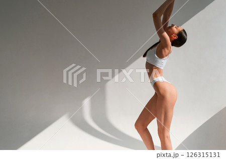 View from the side. Young caucasian woman with slim body shape is indoors in the studio View from the side. Young caucasian woman with slim body shape is indoors in the studio 126315131