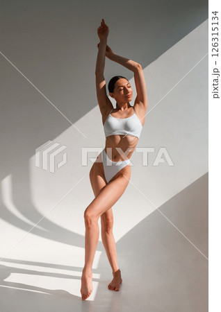 Standing with hands up. Young caucasian woman with slim body shape is indoors in the studio 126315134