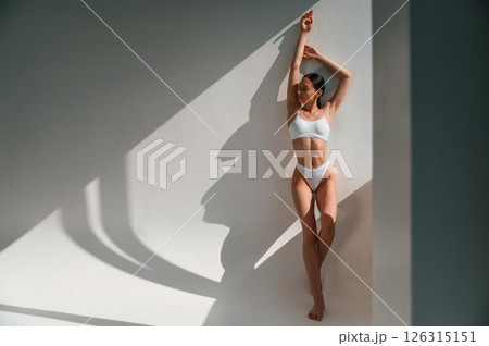 Leaning on the wall. Young caucasian woman with slim body shape is indoors in the studio Leaning on the wall. Young caucasian woman with slim body shape is indoors in the studio 126315151