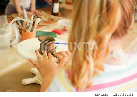 Kids arts and crafts class in workshop. Little girl creating cup and bowl of clay. Creative activity for young children in school. Cute kid forming toy with ceramic. Kids arts and crafts class in workshop. Little girl creating cup and bowl of clay. Creative activity for young children in school. Cute kid forming toy with ceramic. 126315212