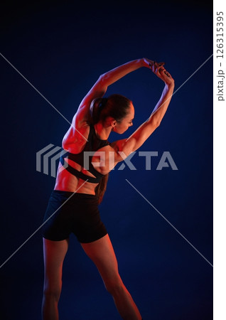 In studio with red and blue neon lighting. Beautiful muscular woman is indoors In studio with red and blue neon lighting. Beautiful muscular woman is indoors 126315395