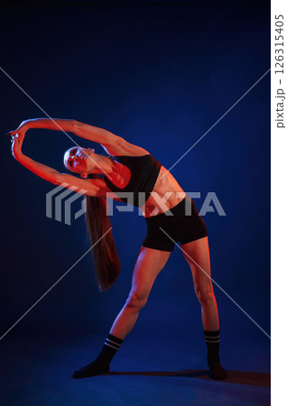 Warm up exercises. Beautiful muscular woman is indoors in the studio with neon lighting Warm up exercises. Beautiful muscular woman is indoors in the studio with neon lighting 126315405