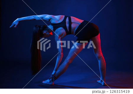 Doing sportive exerises. Beautiful muscular woman is indoors in the studio with neon lighting Doing sportive exerises. Beautiful muscular woman is indoors in the studio with neon lighting 126315419