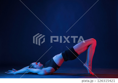 View from the side, lying down on the floor. Beautiful muscular woman is indoors in the studio with neon lighting 126315421