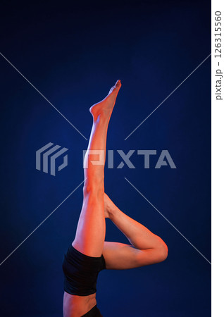 Shoulder stand. Beautiful muscular woman is indoors in the studio with neon lighting Shoulder stand. Beautiful muscular woman is indoors in the studio with neon lighting 126315560
