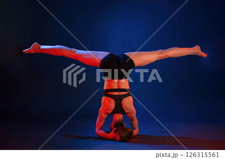 Doing head stand. Beautiful muscular woman is indoors in the studio with neon lighting 126315561
