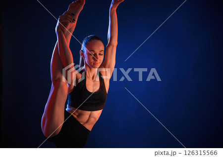 Raising up the leg, exercise. Beautiful muscular woman is indoors in the studio with neon lighting 126315566