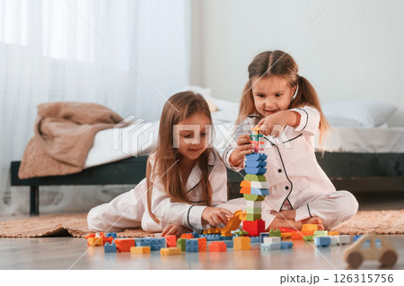Construction toys is on the ground. Two little girls are playing and having fun together in domestic room 126315756