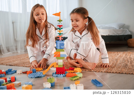 Toy building by construction toys. Two little girls are playing and having fun together in domestic room 126315810