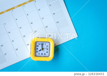 Calendar page and yellow clock on top of blue tabletop. 126316431