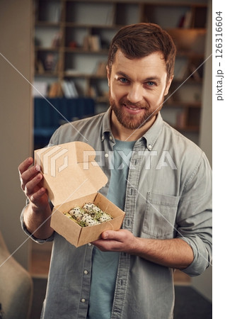 Handsome guy. Man in casual clothes is holding sushi that is in the paper eco box Handsome guy. Man in casual clothes is holding sushi that is in the paper eco box 126316604