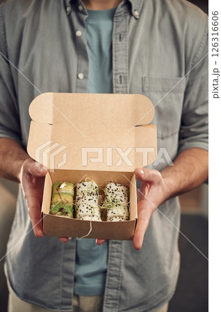 Man in casual clothes is holding sushi that is in the paper eco box Man in casual clothes is holding sushi that is in the paper eco box 126316606
