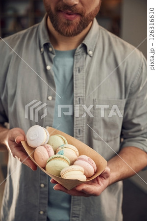 Man in casual clothes is holding macarons that are in the paper eco box. Close up view 126316610