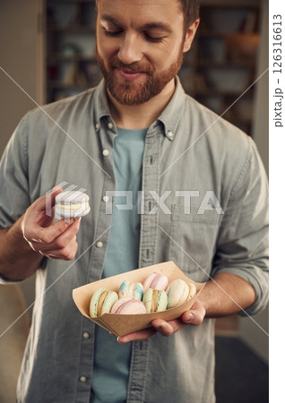 Man in casual clothes is holding macarons that are in the paper eco box. Close up view Man in casual clothes is holding macarons that are in the paper eco box. Close up view 126316613