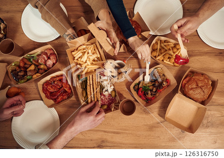 Top view of table with food on it, hands of the people taking it, eating. Meat, vegetables, French fries, burger, mushrooms Top view of table with food on it, hands of the people taking it, eating. Meat, vegetables, French fries, burger, mushrooms 126316750