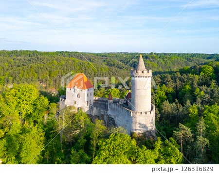 Kokorin Castle stands majestically among lush green trees in Czechia. The aerial perspective captures the serene beauty of the landscape bathed in warm evening light. Kokorin Castle stands majestically among lush green trees in Czechia. The aerial perspective captures the serene beauty of the landscape bathed in warm evening light. 126316829