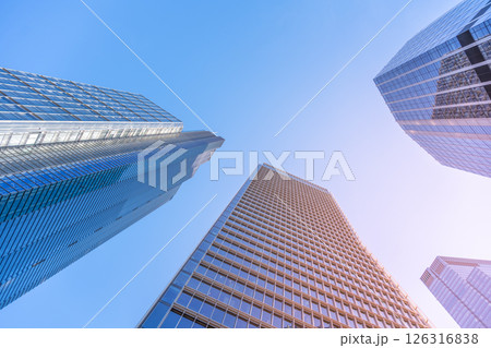Tall, modern skyscrapers rise against a clear blue sky in the City of London financial district. The sunlight reflects off glass facades, highlighting the architectural beauty of the buildings. 126316838
