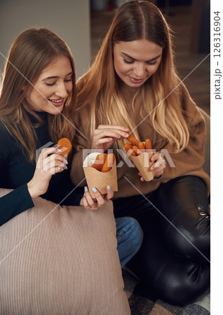 Two women are sitting and eating chicken nuggets indoors together Two women are sitting and eating chicken nuggets indoors together 126316904