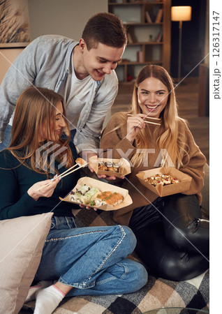 Man with women. Friends are sitting indoors at home and eating sushi together 126317147