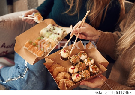 Two women are sitting and eating sushi indoors together Two women are sitting and eating sushi indoors together 126317468