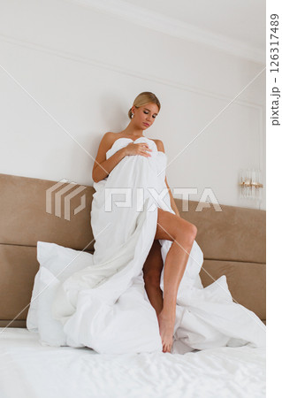 Seductive young bride posing on the bed in hotel room wrapped in white blanket Seductive young bride posing on the bed in hotel room wrapped in white blanket 126317489