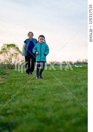 Grandmother and granddaughter enjoying a walk in a green field. A heartwarming moment of family bonding in nature. Grandmother and granddaughter enjoying a walk in a green field. A heartwarming moment of family bonding in nature. 126317516