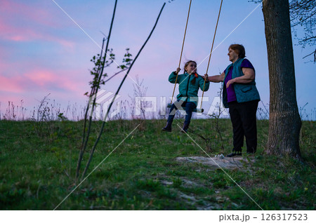 Grandmother and granddaughter enjoying a sunset swing ride. Grandmother and granddaughter enjoying a sunset swing ride. 126317523