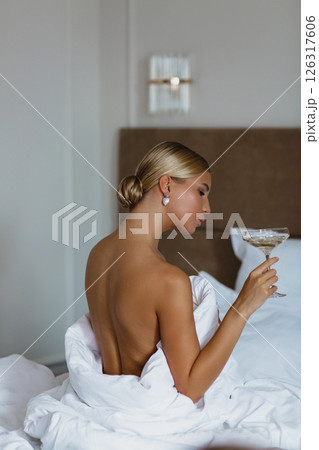 Close-up portrait of a seductive young bride with a glass of champagne, wrapped in a white blanket Close-up portrait of a seductive young bride with a glass of champagne, wrapped in a white blanket 126317606