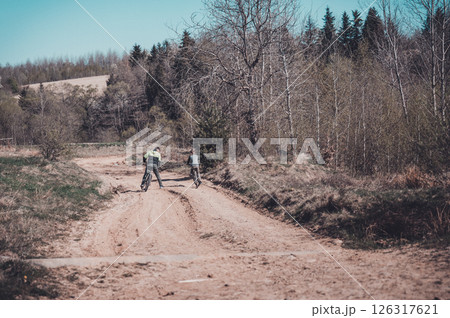 Two cyclists on a dirt path, enjoying a sunny day outdoors. Trees and a forest background. 126317621