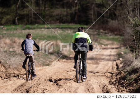 Father and son enjoy a bike ride on a sunny day, traversing a sandy trail through nature. 126317623