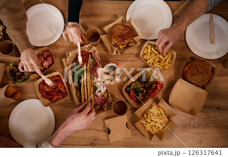Top view of table with food on it, hands of the people taking it, eating. Meat, vegetables, French fries, burger, mushrooms 126317641