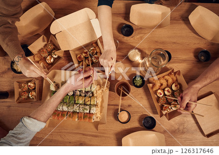 Top view of table with sushi on it in paper eco boxes, hands of the people taking it, eating 126317646