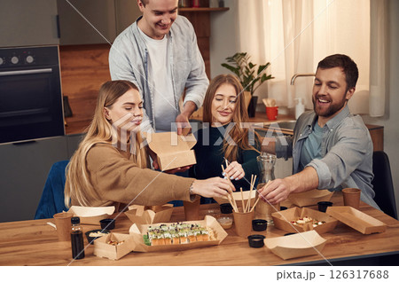 Man is standing. Friends are sitting indoors at home and eating sushi together 126317688