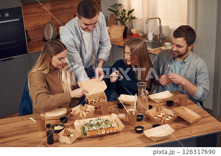 Man is standing. Friends are sitting indoors at home and eating sushi together 126317690