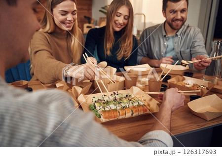 Using chopsticks. Friends are sitting indoors at home and eating sushi together 126317693