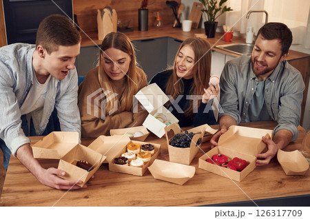 Friends are sitting indoors at home eating macarons, desserts and blueberries together 126317709