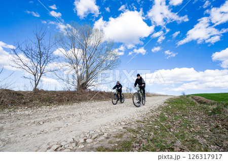 Two cyclists enjoy a sunny day on a gravel path, surrounded by nature's beauty. Two cyclists enjoy a sunny day on a gravel path, surrounded by nature's beauty. 126317917