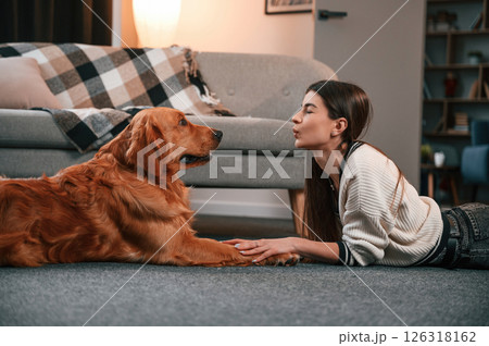 Giving air kiss. Cute golden retriever is in domestic room with his owner, beautiful young woman Giving air kiss. Cute golden retriever is in domestic room with his owner, beautiful young woman 126318162