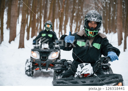 Woman with her friend. Two people are riding ATV in the winter forest Woman with her friend. Two people are riding ATV in the winter forest 126318441