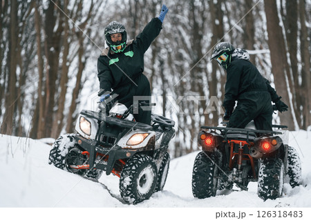 Riding the opposite ways. Two people are on the ATV in the winter forest Riding the opposite ways. Two people are on the ATV in the winter forest 126318483