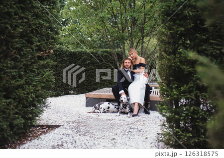 Stylish young beautiful newlywed couple walking at wedding in park with two dalmatians Stylish young beautiful newlywed couple walking at wedding in park with two dalmatians 126318575