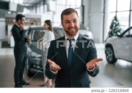 Beautiful man is standing and smiling. Three people are working together in the car showroom 126318868
